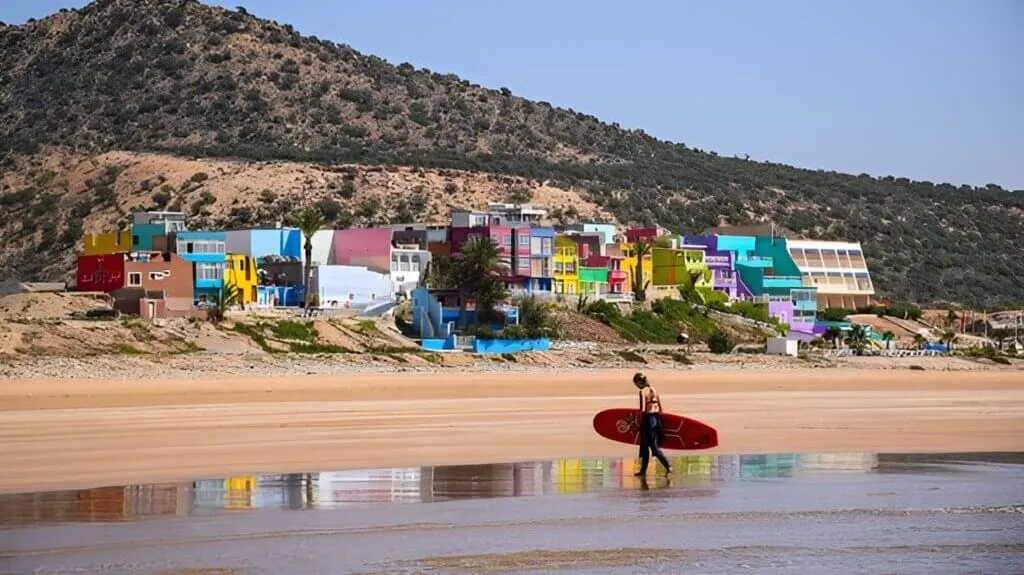 Village coloré d'Aghroud vu depuis la plage avec une surfeuse